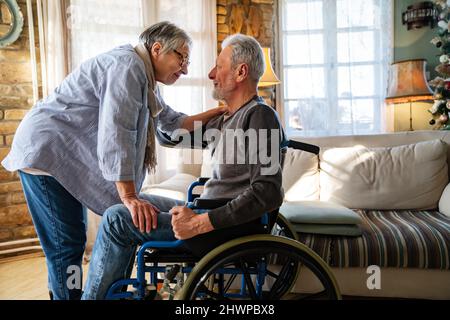 Mature man with disability in wheelchair spending time together with his wife at home Stock Photo