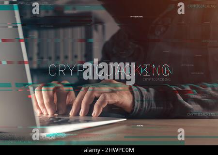 Cryptojacking concept with faceless hooded hacker working on laptop computer, with glitch effect and selective focus Stock Photo