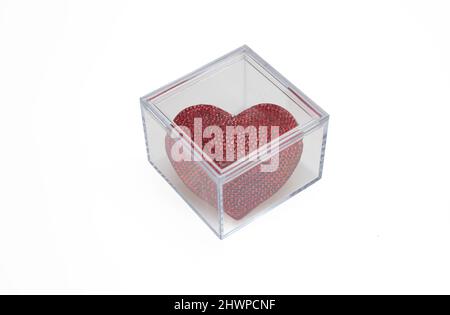 Cube of glass with red color ruby heart shape jewel isolated cutout on white background. Overhead view of transparent square box with love symbol, ann Stock Photo