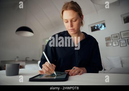 Caucasian female fashion designer working from home designing garments on digital tablet  Stock Photo