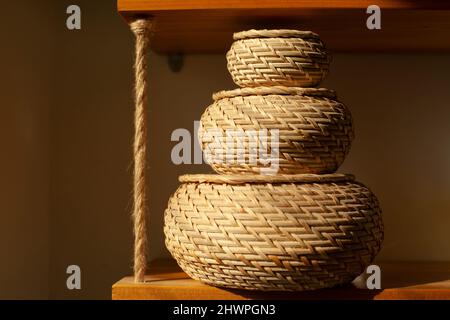 Basket for small things. Object in interior. Braided box is rounded in shape. Sunlight on object in room. Three boxes stand on top of each other. Stock Photo