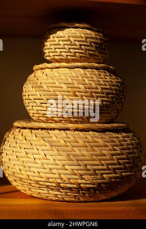 Basket for small things. Object in interior. Braided box is rounded in shape. Sunlight on object in room. Three boxes stand on top of each other. Stock Photo