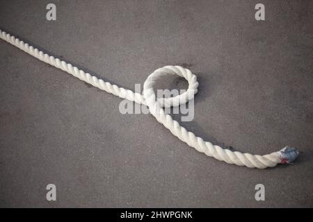 The end of the rope. The rope lies on the ground. Long rope on the pavement. Muscle training equipment. Ship mooring rope. Stock Photo