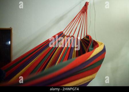 Fabric hammock on ropes. Thing for relaxation. Details of interior hammock in apartment. Multi-colored fabric. Place to sleep. Stock Photo