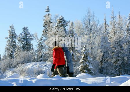 Couple wearing heavy Winter Clothing, enjoying a walk on beautiful winter day with freezing temperature below 25 Degree Celsius., near Smithers, Inter Stock Photo