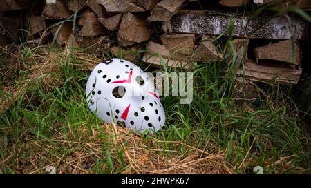 Creepy white hockey mask lays on the ground near with woods Stock Photo