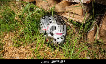 Creepy steel hockey mask lays on the ground near with woods Stock Photo