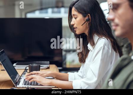 Young businesswoman using laptop by businessman at desk in coworking office Stock Photo