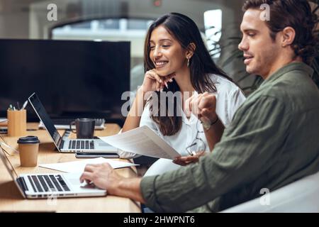 Smiling businessman and businesswoman discussing over documents and laptop at desk in coworking office Stock Photo