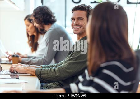 Smiling businessman sitting with colleagues at desk in coworking office Stock Photo