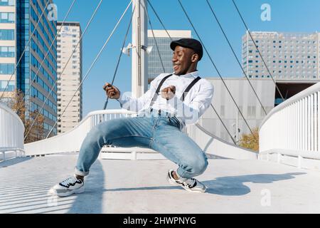 Cheerful young man with cap dancing on bridge Stock Photo