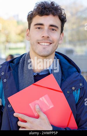 Smiling man with red file at campus Stock Photo