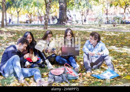 Happy students using smart phone and laptop in college park Stock Photo