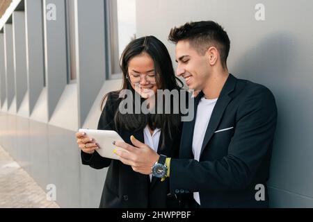 Multiracial business colleagues using tablet PC leaning on wall Stock Photo