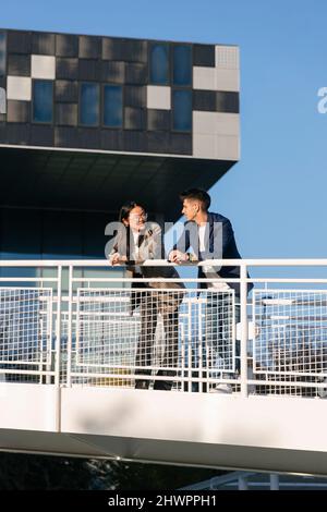 Business colleagues talking to each other leaning on railing Stock Photo