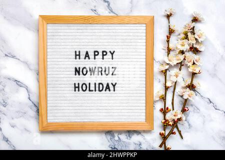 Sprigs of the apricot tree with flowers and Text Happy Nowruz Holiday Concept of spring came Top view Flat lay Hello march, april, may, persian new ye Stock Photo