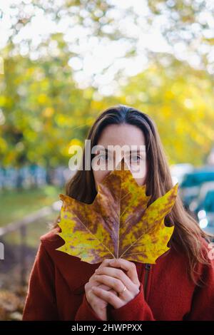 Portrait of woman holding autumn leaf in front of her face Stock Photo ...