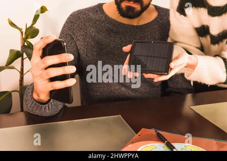 Businesswoman showing solar panel on video call by businessman holding smart phone Stock Photo