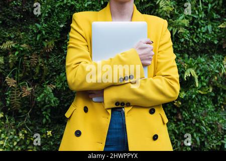 Businesswoman in yellow jacket holding laptop at park Stock Photo