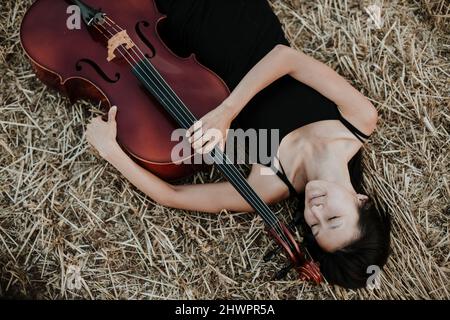 Woman with cello lying in stubble field Stock Photo