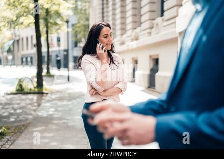 Smiling businesswoman talking on mobile phone at footpath Stock Photo