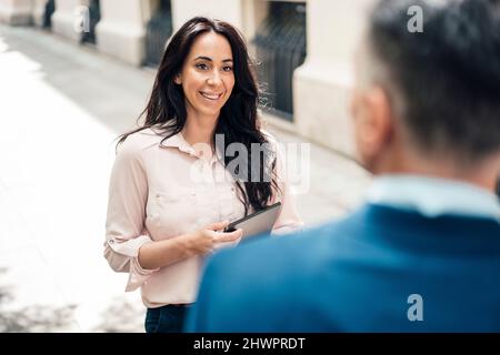Happy businesswoman talking with businessman on footpath Stock Photo