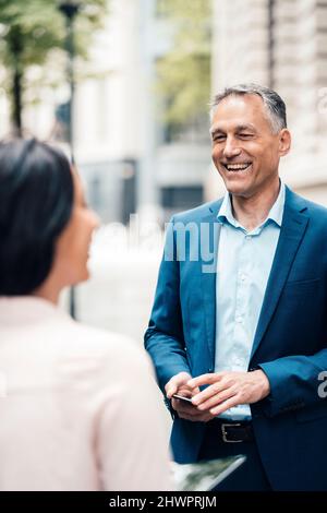 Cheerful mature businessman talking with businesswoman on footpath Stock Photo