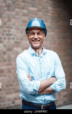 Happy mature architect standing with arms crossed in front of wall Stock Photo