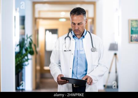 Mature doctor examining medical record on tablet PC in hospital Stock Photo