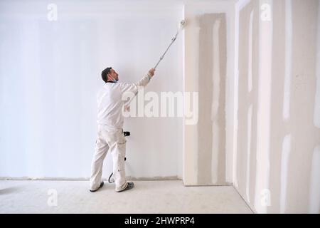 Painter painting wall with roller at construction site Stock Photo