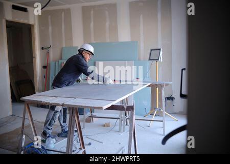 Construction worker measuring sheetrock on workbench at site Stock Photo