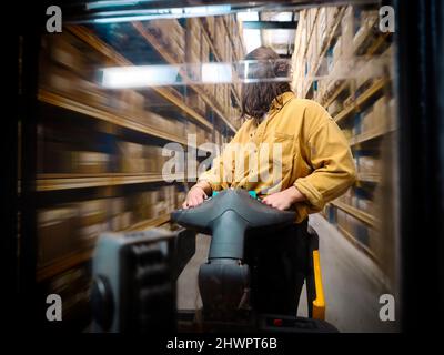 Warehouse worker looking back pushing hand truck in alley Stock Photo