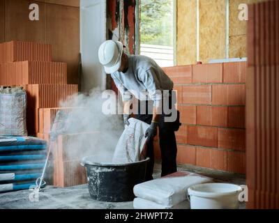 Bricklayer putting cement in tub at construction site Stock Photo