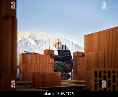 Bricklayer fixing bricks crouching at construction site Stock Photo