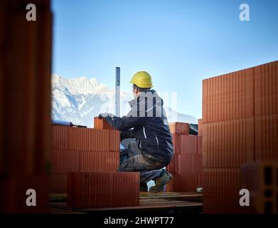 Bricklayer using spirit level on stacked bricks crouching at construction site Stock Photo