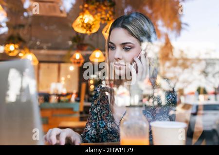 Woman using smart phone and using laptop in cafe Stock Photo