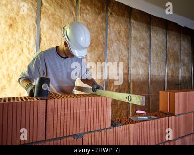Bricklayer with hammer using spirit level on bricks at construction site Stock Photo