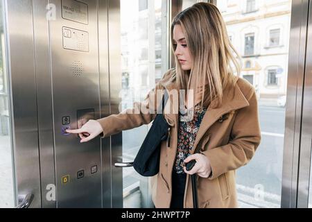 Blond woman pressing button in elevator Stock Photo