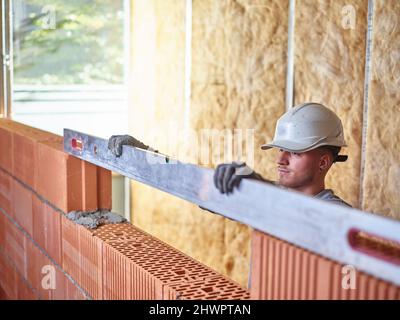 Concentrated bricklayer using spirit level to measure bricks at construction site Stock Photo