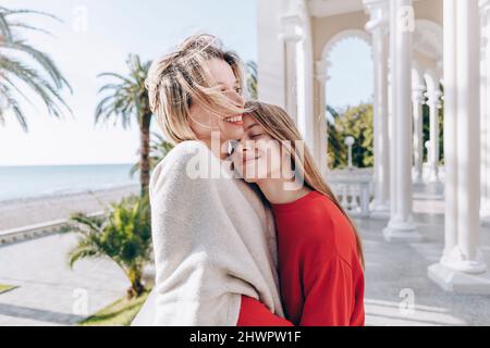 Smiling teenage girl with eyes closed embracing mother on sunny day Stock Photo