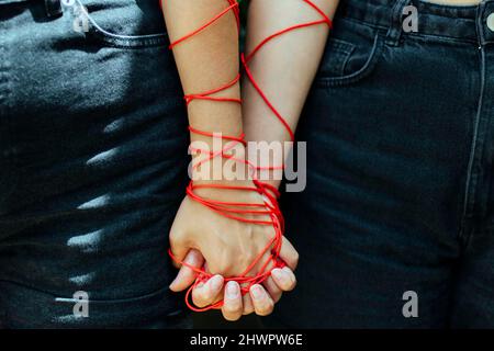 Two women with thread holding hands Stock Photo