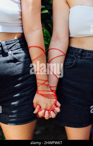 Two women with thread holding hands Stock Photo