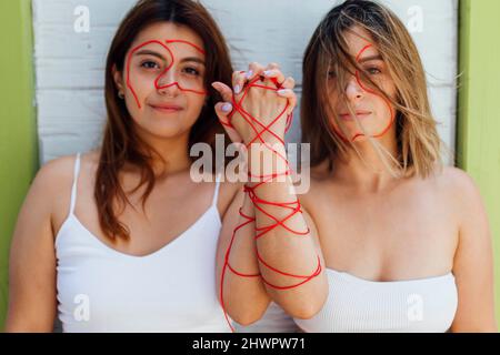Young women with thread holding hands in front of wall Stock Photo