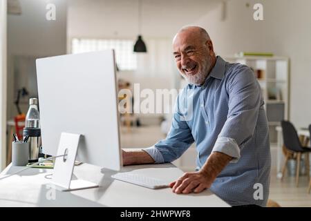 Cheerful senior freelancer with computer working from home Stock Photo