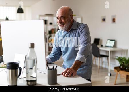 Cheerful senior businessman using computer at desk Stock Photo