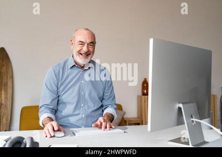 Happy senior freelancer with computer sitting at desk Stock Photo