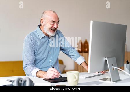 Cheerful freelancer using graphic tablet and computer at desk in home office Stock Photo
