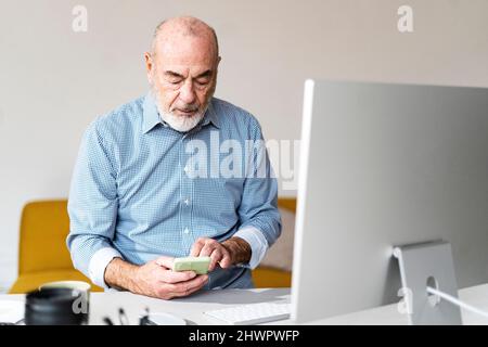 Freelancer text messaging through smart phone in home office Stock Photo