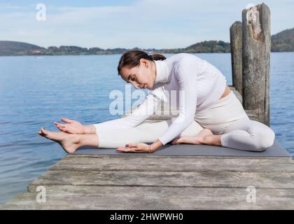 Woman doing stretching exercise on jetty at lake Stock Photo