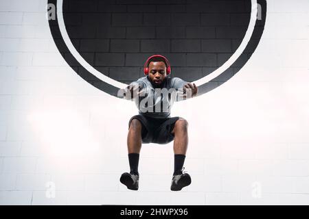 Young sportsman with headphones jumping in front of white wall Stock Photo